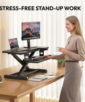 Sanodesk 35 Inch Electric Height Adjustable Standing Desk Converter Riser With Large Keyboard Tray Ergonomic Sit Stand Monitor Workstation For Home Office Black Color Ready To Use Out Of Box Fast Assembly in use with a user standing, holding a coffee.