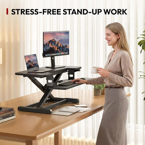 Sanodesk 35 Inch Electric Height Adjustable Standing Desk Converter Riser With Large Keyboard Tray Ergonomic Sit Stand Monitor Workstation For Home Office Black Color Ready To Use Out Of Box Fast Assembly in use with a user standing, holding a coffee.
