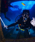 Scuba diver inside shipwreck holding action camera, brightly colored fish swimming with durable scuba gear retractor with carabiner