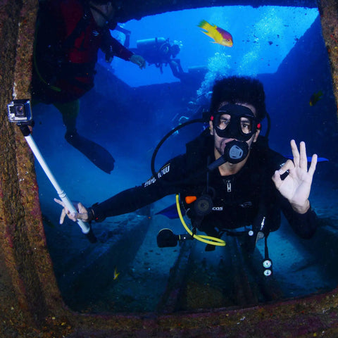 Scuba diver inside shipwreck holding action camera, brightly colored fish swimming with durable scuba gear retractor with carabiner