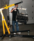 Heavy Duty Rolling Boom Engine Hoist With Two Thousand Pounds Capacity Fold Up Legs And Smooth Swivel Casters That Make Tight Garages A Breeze For Every Weekend Wizard Industrial Grade Steel Construction in use lifting an engine block.