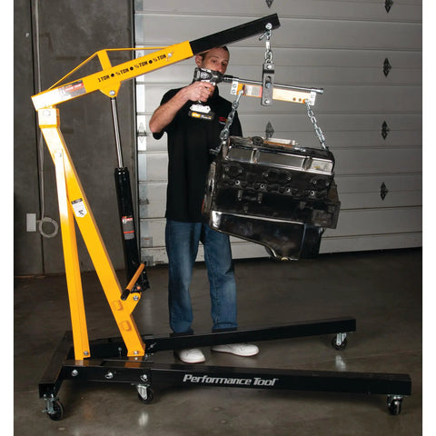 Heavy Duty Rolling Boom Engine Hoist With Two Thousand Pounds Capacity Fold Up Legs And Smooth Swivel Casters That Make Tight Garages A Breeze For Every Weekend Wizard Industrial Grade Steel Construction in use lifting an engine block.