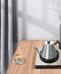 Commercial Stainless Steel Single Cup Warmer With 80W Heating Plate Keeps Your Daily Brew Hot All Day Long Non Stick Surface That Honestly Hits Different For Home Office Or Cafe Use on a wooden table with a coffee cup.