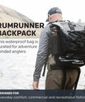 Rum Runner Gage Tech Waterproof Backpack For Fishing And Outdoors Angler Gear Carrier, worn by person by river.