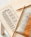 Quick Gauge Ruler For Knitting And Crochet No Sweat Stitch Measurement Tool With Clear Grid Layout on table with yarn and knitting needles.