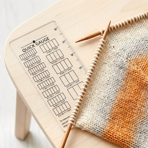 Quick Gauge Ruler For Knitting And Crochet No Sweat Stitch Measurement Tool With Clear Grid Layout on table with yarn and knitting needles.