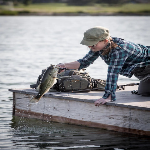 Angler using Ultra Lightweight Fly Fishing Vest With 14 Pockets And Front Zip Storage Olive Green on dock, holding caught fish.