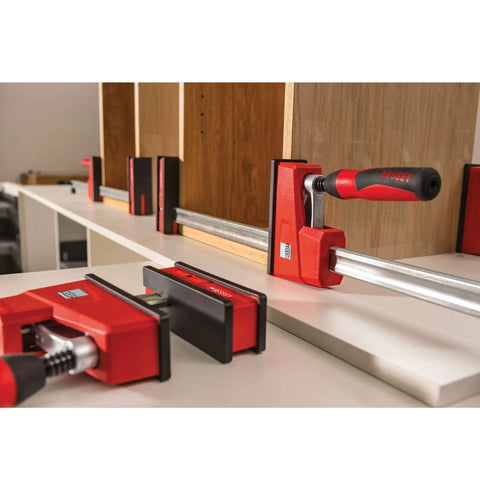 Heavy Duty 40 Inch Parallel Clamp Delivering 1700 Lbs Of Tight Grip For Woodworking Cabinetry viewed on a workbench with wooden panels.
