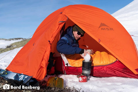 Camper using Windproof Camping Stove System With Radiant Burner And Regulator Fast Boil 1.8 Liter Pot inside orange tent.