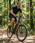 Person riding an e-bike through a forest, showcasing the Mid Drive Spider Adapter Ring For 130BCD Aluminum Alloy Chainring Adapter.