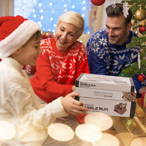 Family exchanging Motorized Marble Run Set with Spaceport and Night City Tracks under Christmas tree, showing gift packaging.