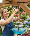 Woman installing Blue Hanging Solar Powered Bird Bath Fountain With Solar Pump For Outdoor Patio Backyard Lawn Garden Decor No Wires Easy Setup Gentle Water Cascade To Attract Birds And Create A Tranquil Yard Oasis No Fuss.