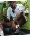 Camper holding Multifunctional Orienteering Compass With Luminous Pointer Scale Ruler And Mirror, seated near a green tent.