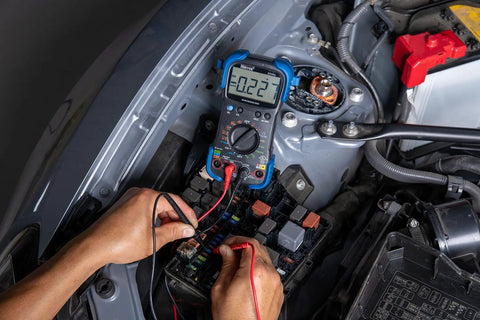 Hands using pro grade automotive digital multimeter with auto range and overload protection in car engine diagnostics