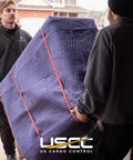 Two movers carrying a furniture piece wrapped in heavy duty moving blankets 72x80 4 pack blue polyester quilted furniture pads.