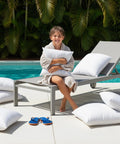 Child sitting on lounge chair with Outdoor Pillow Inserts 18 By 18 Inches Pack Of 2 White No Fuss Water Resistant Throw Pillows by the pool.