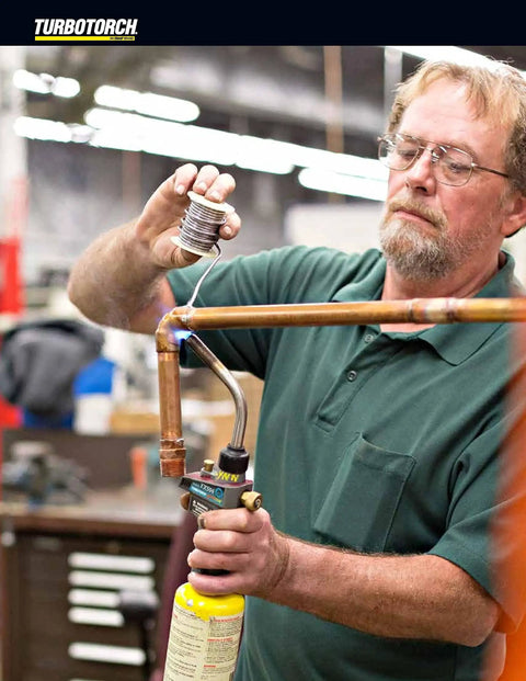 Person using Self Lighting Hand Torch TX504 With Extreme Swirl Technology for brazing copper pipes in workshop setting.