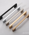 Four rectangular cabinet pulls in black, silver, bronze, and gold on a flat surface, showcasing different finishes and styles.