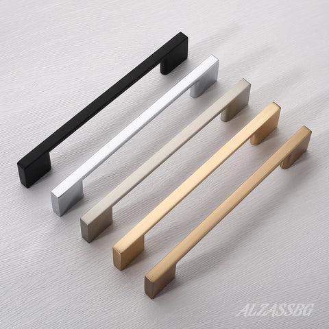 Four rectangular cabinet pulls in black, silver, bronze, and gold on a flat surface, showcasing different finishes and styles.