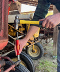 Grease Buster grease-fitting cleaner with red handle used on a tractor grease fitting; yellow mallet in background