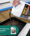 Solid Color Wood Stain For Decks And Fences UV Resistant Opaque Finish That Hides Imperfections Long Lasting Exterior Paint With Zinc Nano UV Protection 1 Gallon being poured into a paint tray.