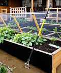 Long Reach 4-In-1 Garden Hoe With 64 Inch Handle for Easy Weeding leaning on raised garden bed