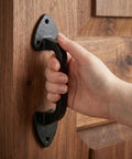 Hand gripping Rustic Cast Iron Outdoor Gate Handle on wooden door, part of 3 Pack with Ergonomic Grip Sliding Barn Door Pulls for Garage and Fence.