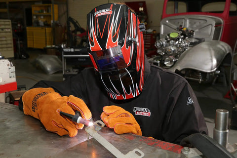 Person welding with protective helmet and gloves, wearing Black Flame-Resistant 9 Oz Cotton Welding Jacket Delivers Breathable Comfort, Large Size, Shields Arms And Torso From Spatter And Heat, Snap Cuffs For A Snug Fit, Internal Pocket For Safe Storage, Tough As Nails Weld Gear For Daily Use