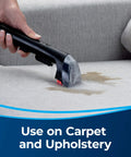 Close-up of a black Bissell 3-inch tough stain tool cleaning upholstery on a sofa