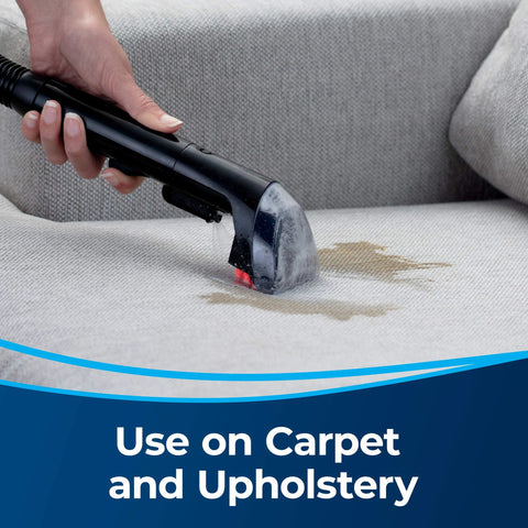 Close-up of a black Bissell 3-inch tough stain tool cleaning upholstery on a sofa