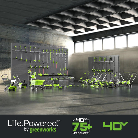 Various Greenworks yard tools displayed against a wall, including mowers, blowers, and trimmers under overhead lighting.