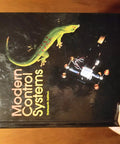 Cover of Modern Control Systems textbook with gecko illustration and electronics on a wooden table surface.