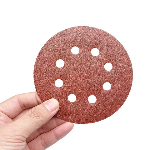 Hand holding a disc from 35 Piece 5 Inch Sanding Discs Set With 8 Hole Pattern Hook And Loop, 7 Grits 60 80 100 120 150 180 240 For Random Orbital Sander