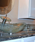 Clear Glass Oval Slipper Vessel Sink Set With Slick Brushed Nickel Hardware Tempered Glass Scratch Resistant Finish One Point Five Inch Brass Pop Up Drain Includes Mounting Ring Perfect Modern Vanity Centerpiece on granite countertop.