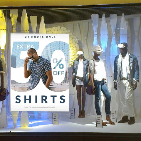 Store window display with mannequins dressed in casual summer outfits and a sign advertising 'Shirts 50% Off, 24 Hours Only'