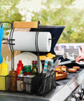 Grill Caddy With Paper Towel Holder And Seven Compartment Organizer For Outdoor BBQs, utensils, condiments on a barbecue grill.