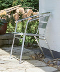 Aluminum chair placed on patio near brick wall and potted plants, showing outdoor setting.