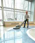 Person using automatic floor machine with red 20 inch floor scrub pad for spray buffing and light cleaning in bright lobby
