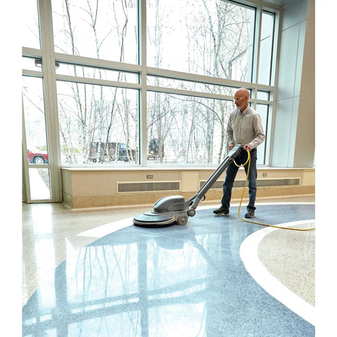 Person using automatic floor machine with red 20 inch floor scrub pad for spray buffing and light cleaning in bright lobby