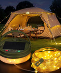 Solar Camping String Lights 33ft 100 LED With 9 Modes USB C Rechargeable illuminating a tent and table with chairs at night.