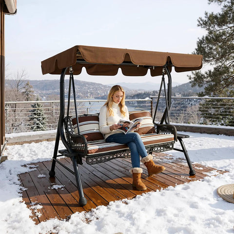 Woman reading on a three seat outdoor patio swing chair with large convertible canopy porch glider hammock lounge chair for porch rattan wicker steel frame cushions and pillows brown, on a snowy deck.
