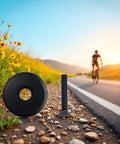 Black Front Fork Stem Top Cap And Screw for 1-1/8 inch road bike stems placed on roadside with bike and flowers in background.
