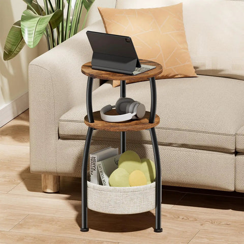 3 Tier Round Side Table With Storage Basket 24 Inch Tall Rustic Brown Space Saving End Table For Tight Spaces Sofa Side Table Or Nightstand Dorm Organizer Patio Drink Table For Living Room And Bedroom next to couch with tablet and headphones.