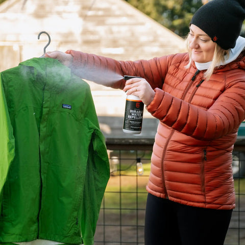 Person using Revivex DWR Spray For Waterproof Jackets And Rain Gear Keeps Your Gear Dry And Gore-Tex Breathable With Water Beading Again Restore Waterproofing For Tents Camping Gear And Winter Wear For Real World Adventures on green jacket outdoors.
