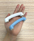 Hand holding two ceramic cabinet pulls, white glossy and light blue, showcasing design and size contrast.