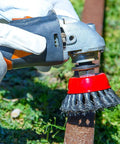 Side view of angle grinder with red-hub wire wheel brush attached and carbon steel bristles cleaning rust from metal pipe