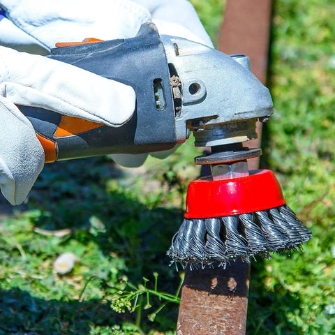 Side view of angle grinder with red-hub wire wheel brush attached and carbon steel bristles cleaning rust from metal pipe