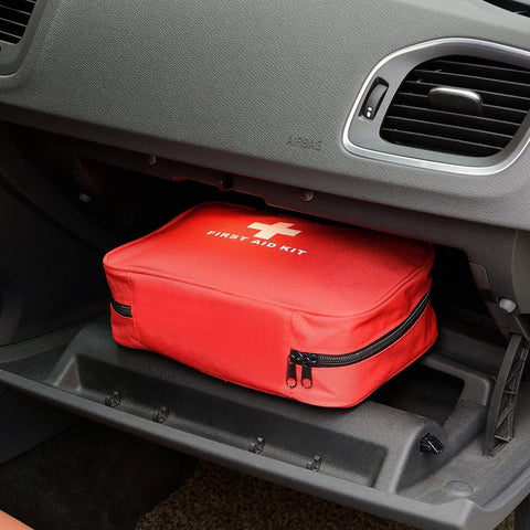 Red compact first aid kit bag with white cross, zippered, in car glove compartment (front view)