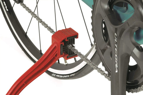 Grunge Brush Bike Chain And Gear Cleaner With Dual Sided Bristles cleaning bike chain and cassette, attached to rear wheel.