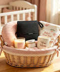 Wicker basket in nursery with pink cushion, candle, black pouch, mug labeled 'New Mom,' and baby blanket.